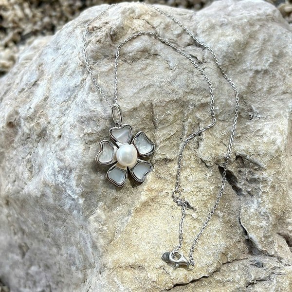 Delicate pearl flower necklace on a silver chain, displayed on a natural surface.
