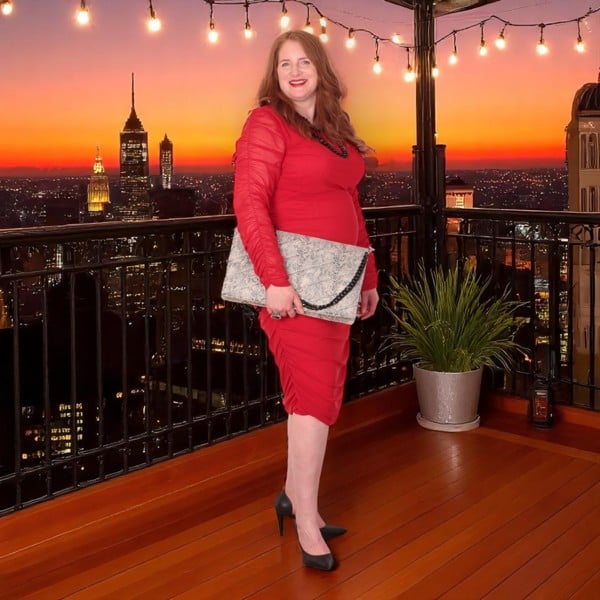 Model is wearing a red dress and  a snake print quilted laptop clutch bag with chain strap. Rooftop Bar Background