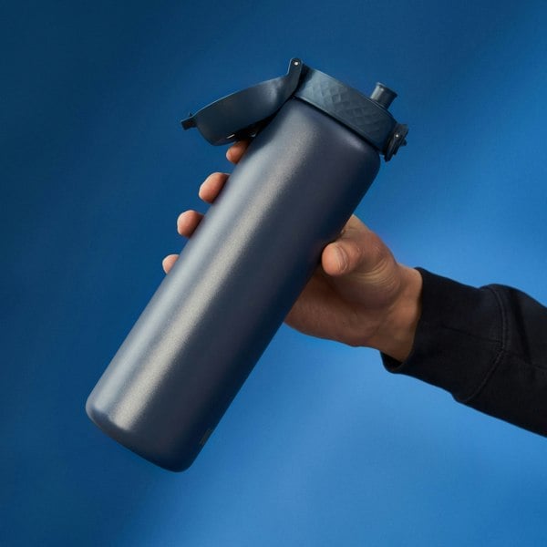 A dark-blue water bottle is held by a hand, against a blue background.