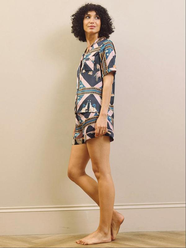 Woman wearing a patterned dress standing against a plain wall.