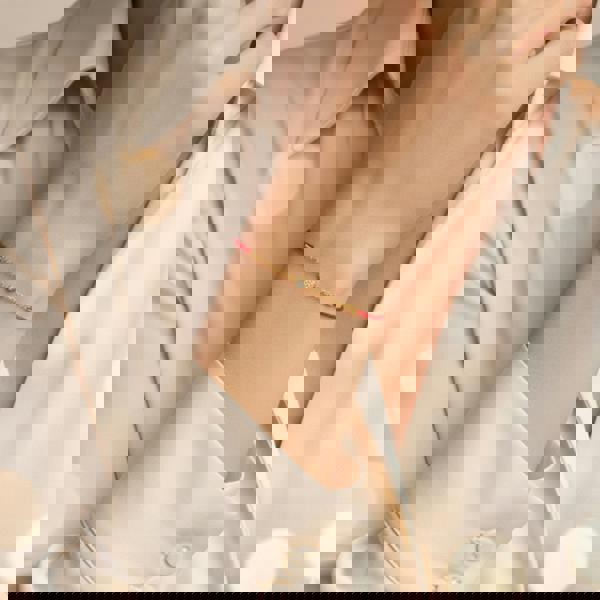 Gold bracelet with a red string worn on a wrist against a light background. Heart_silk_cord_gold_bracelet_perfect_for_gifting