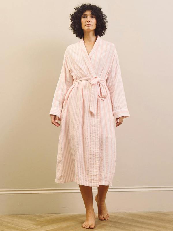 Woman wearing a pink striped pyjama set and robe against a plain background