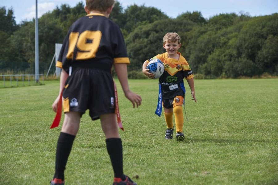 Young player running with ball in blue Optimum tag belt toward a defender in red flags, on grass