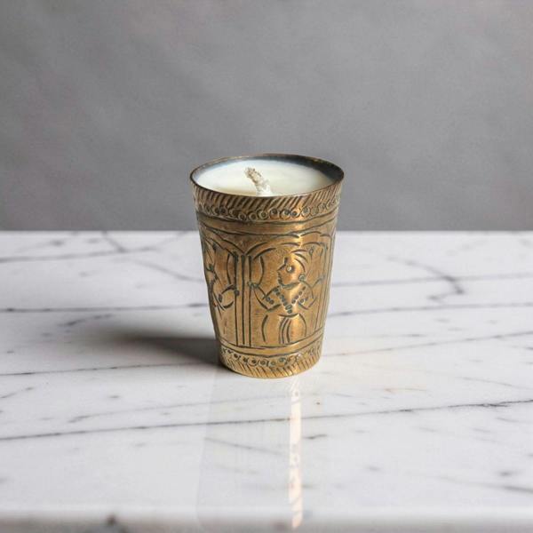 Decorative candle in an ornate brass holder on a marble surface with a gray background
