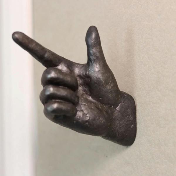 An antiqued dark bronze polyresin coat hook shaped like a pointing finger hand, mounted on a light grey plaster wall.