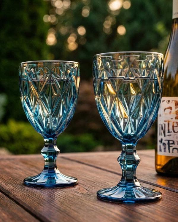 Two blue glass goblets and a bottle on a wooden surface with a blurred natural background