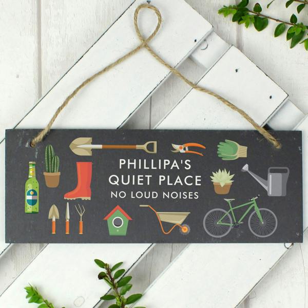 A rectangular hand-cut dark slate sign with rustic hanging twine, colourful garden illustrations, and custom uppercase text reading Mum's Garden Quiet Zone.