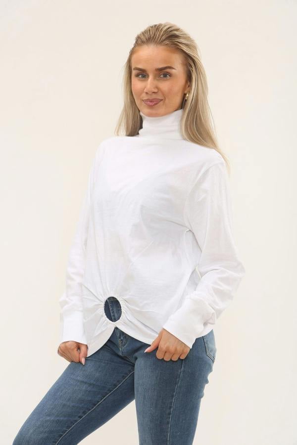 Woman wearing a white turtleneck sweater and blue jeans against a plain background