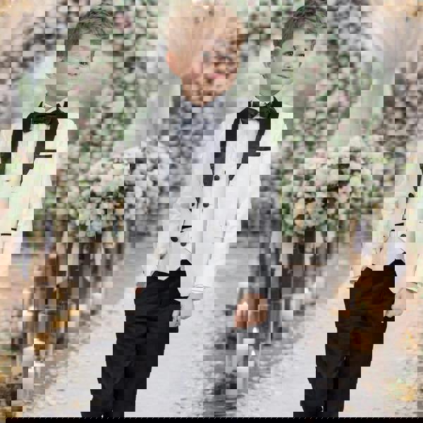 Young boy in a formal outfit walking down a decorated wedding aisle with flowers and candles.