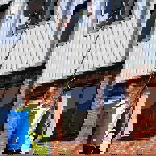 16L blue water fed backpack with green cleaning pole reaching a window, worker in safety vest, brick wall background