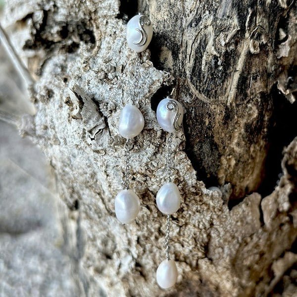 Shimmering pearl earrings with flowing chain and accents, displayed on a tree trunk.