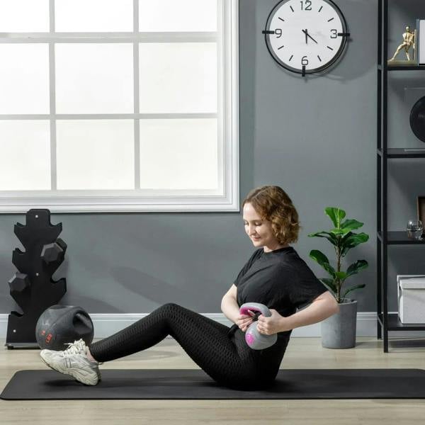 Pink and grey kettlebell held while kneeling on a workout mat for strength
