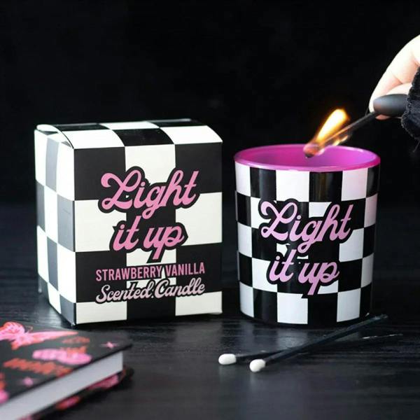 Scented candle in black-and-white checkered jar with pink wax, lit flame