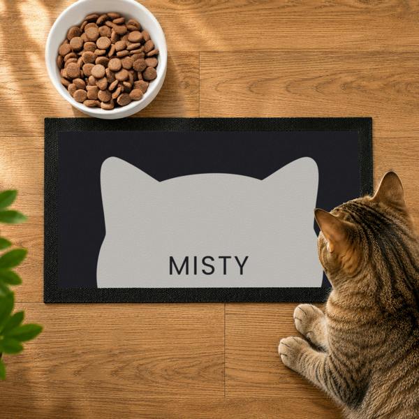 Top-down view of a black personalised cat bowl mat featuring a grey cat silhouette graphic and the name MISTY.