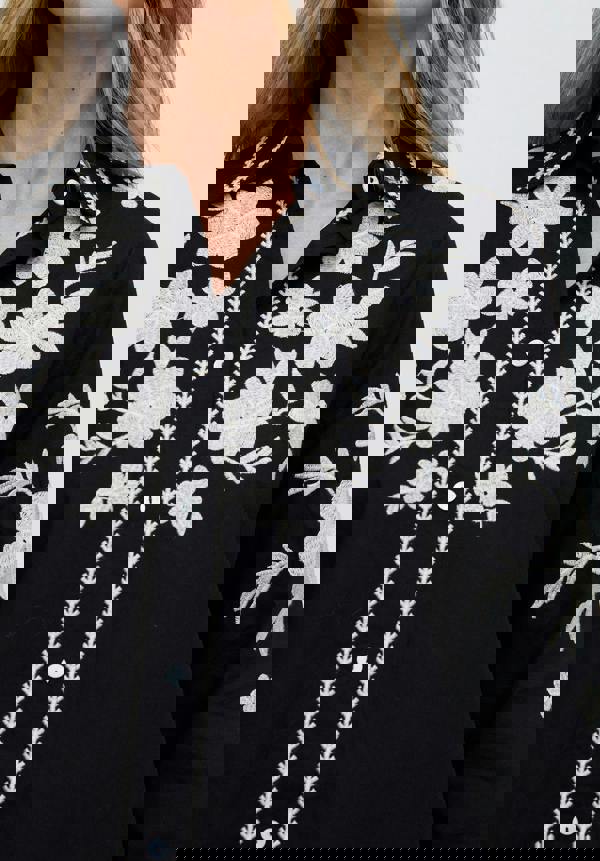 Black shirt with white floral embroidery on a plain background