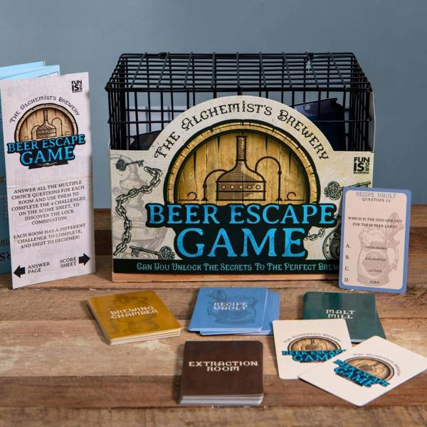A tabletop Beer Escape Room Game kit displayed on a wooden surface, featuring a black wire metal cage, a guide for 'The Alchemist's Brewery', and various game cards labeled 'Brewing Chamber', 'Recipe Vault', and 'Malt Mill'.