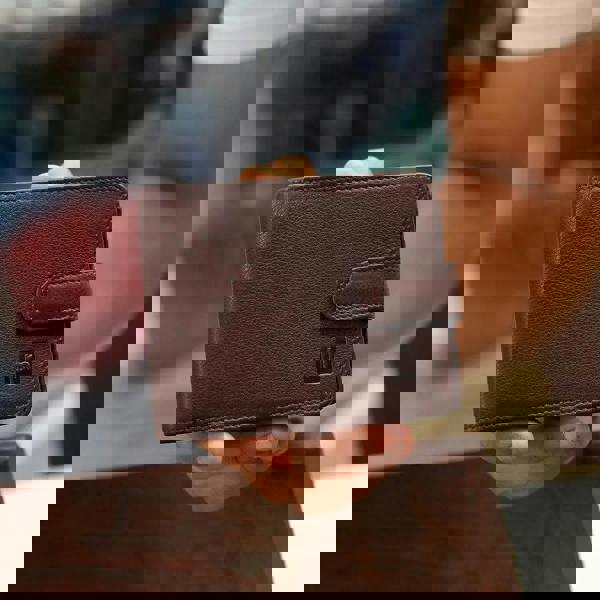 Brown leather wallet held by a person with a blurred background