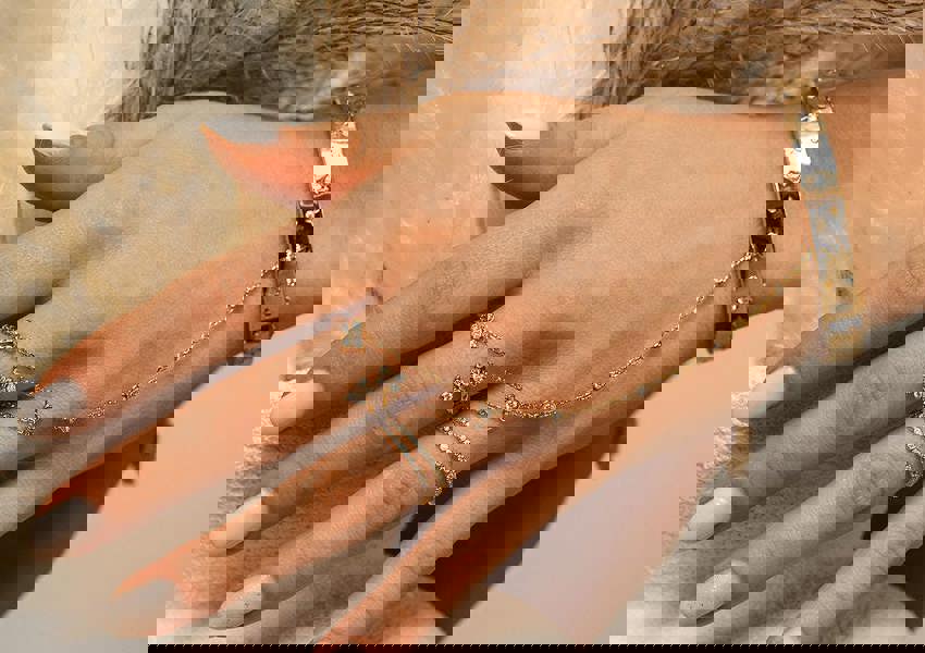 Hand wearing gold jewelry with a neutral background. Adjustable sterling silver finger chain by BLOOMTINE with 6 lab-grown diamonds. Known as a hand harness or slave bracelet, this tarnish-resistant rhodium-plated piece features a diamond-cut chain for maximum light refraction. An ethical, high-sparkle luxury gift