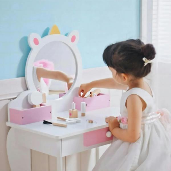 Kids unicorn dressing table with round mirror, pink drawers, and tabletop makeup accessories.
