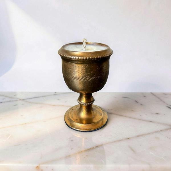 Bronze candle holder with a lit candle on a marble surface