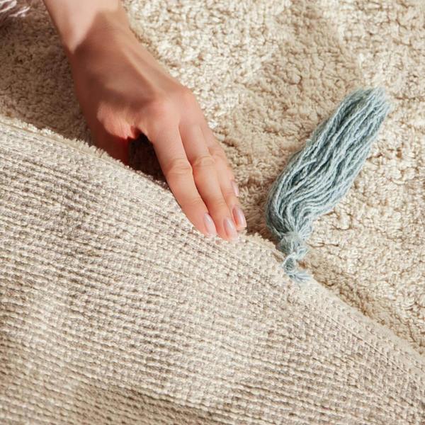 Hand touching a textured beige surface with a blue tassel