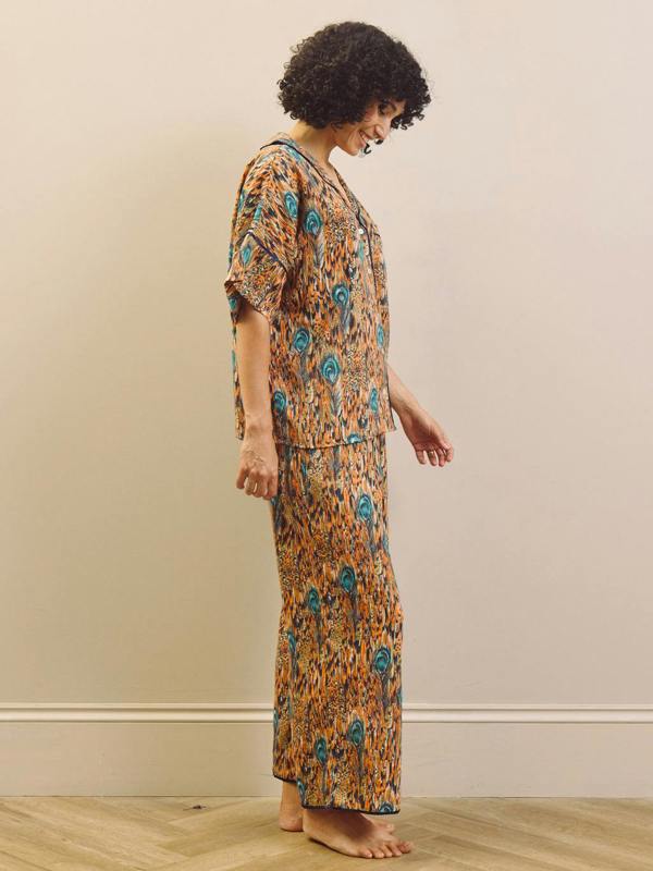 Woman wearing a patterned feather print pyjama set standing against a plain wall.