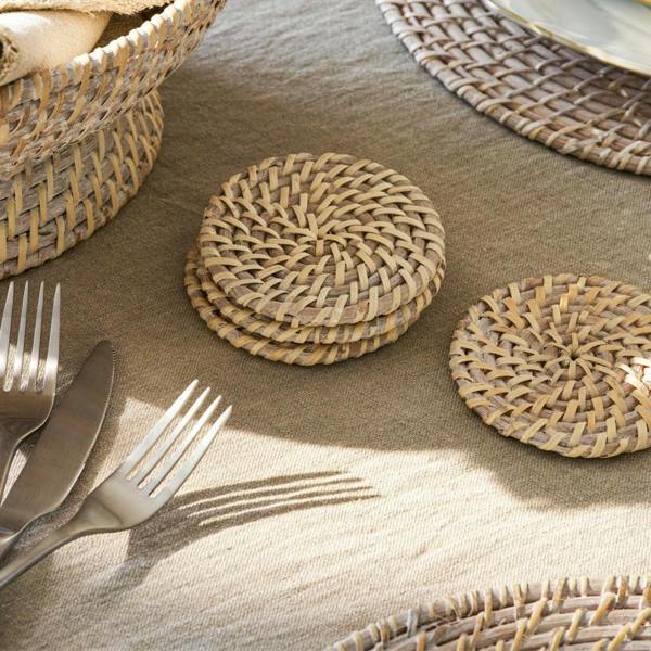 A stack of four round whitewash rattan coasters on a linen-covered table.