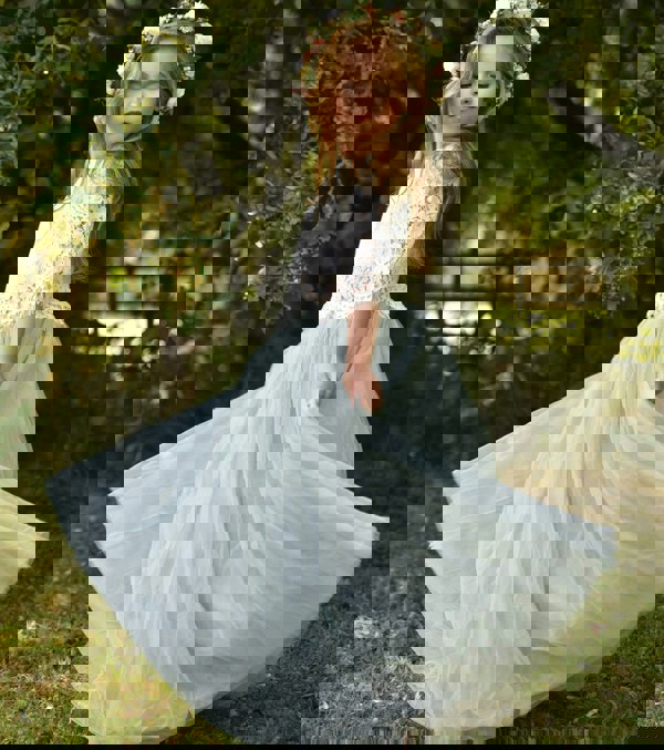 Young girl in a white lace top and light green tulle skirt with a floral crown outdoors.