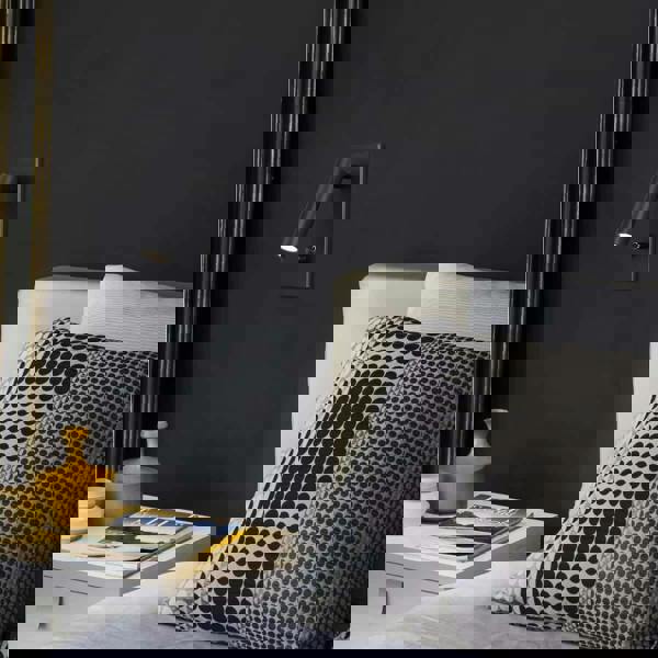 black dimmable reading light mounted on a black wall next to a bed