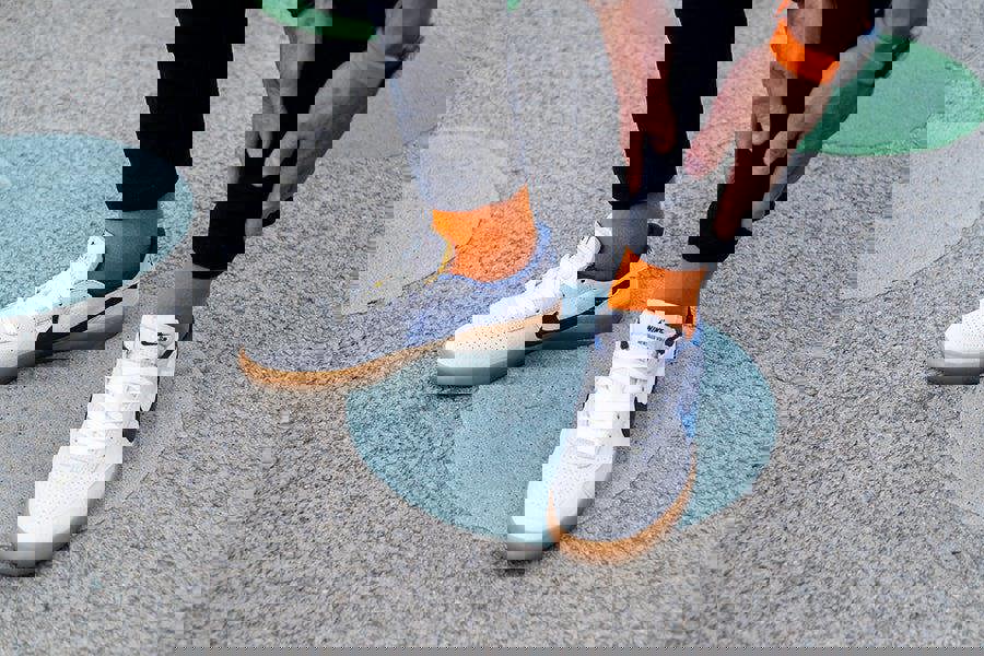 Person wearing white sneakers with blue swooshes, orange socks, and black levi jeans on a concrete surface.