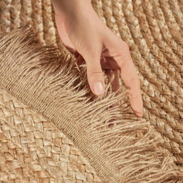 Hand touching a woven brown rug with fringes
