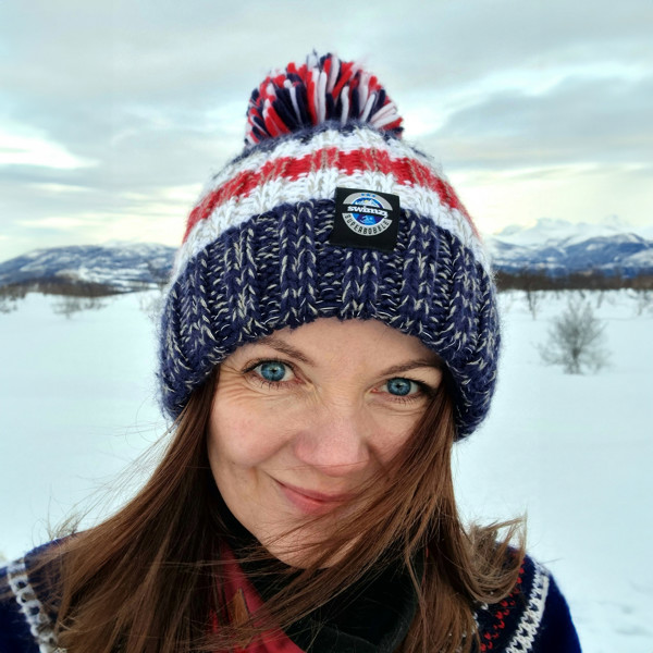 Women in a Scandinavian frozen landscape is wearing a stylish dark navy, white and red striped chunky Super Bobble hat with a large pom-pom and a deep ribbed headband. The hat contains reflective yarns and is lined in luxury sherpa fleece.