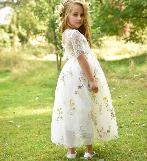 Young girl in a white floral dress standing in a grassy field.