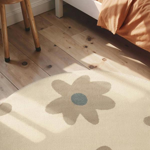 Round beige rug with a flower design on a wooden floor.