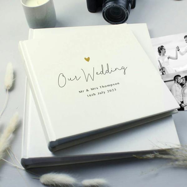 Personalised square photo album with gold heart and Our Wedding inscription resting on a grey surface