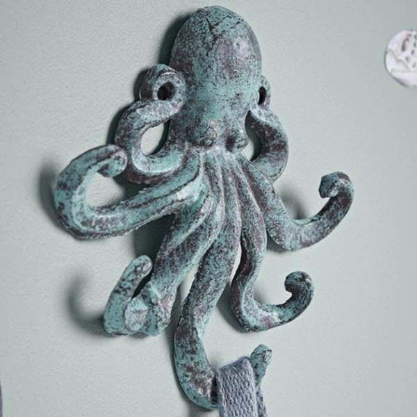 A close-up side view of a textured teal and copper-effect Octopus Hook mounted to a sage green wall holding a fabric loop.