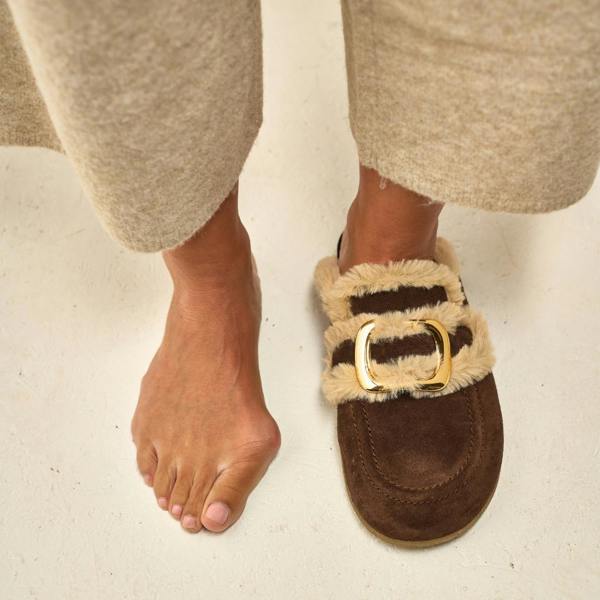 Brown slipper with gold buckle worn by a person on a light background