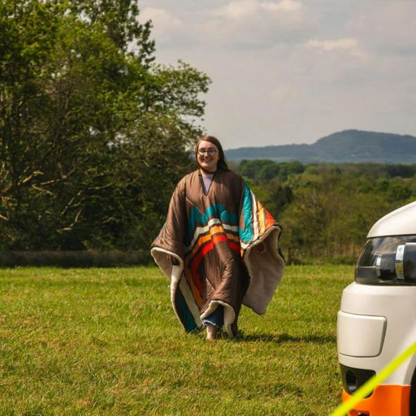 a young lady walking towards a camper van wearing the Vivid Spruce Insulated Outdoor Blanko Blanket as a poncho. imageset:Vivid Spruce