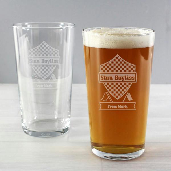 An empty and a filled personalised Formula One pint glass showing custom laser etching with the name Stan Bayliss and message From Mark on a light wooden table.