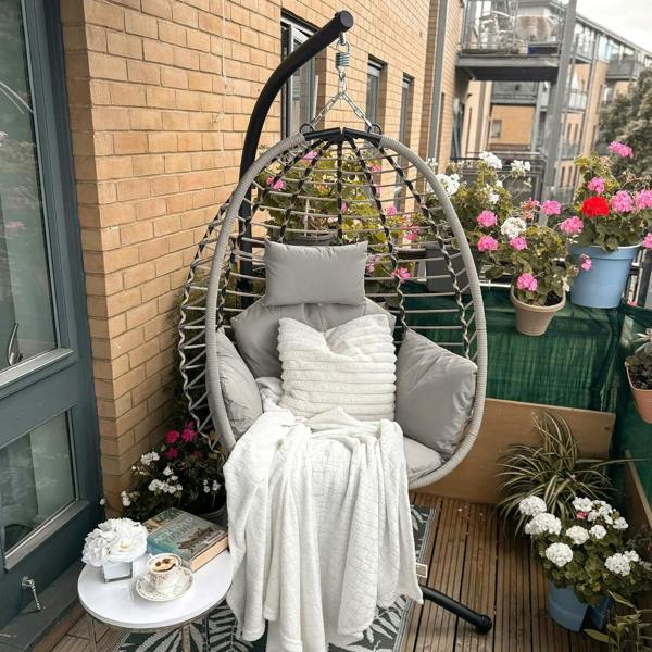 Grey hanging egg chair with padded cushions on black stand, shown with throws
