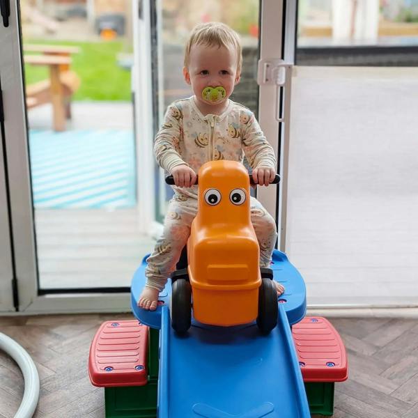 Toddler riding orange ride-on car on blue roller coaster base with green steps