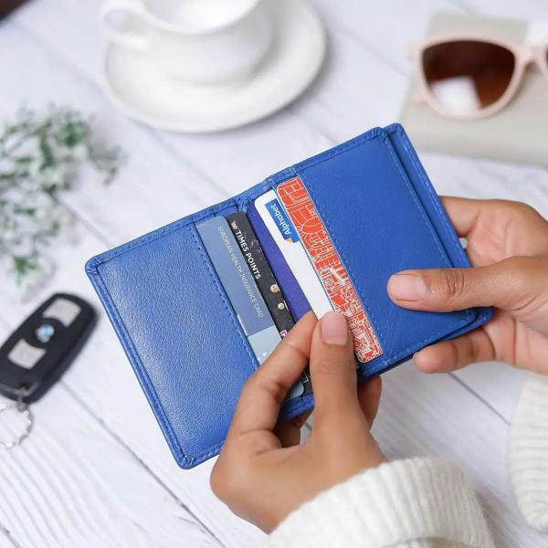 Person holding a blue wallet with cards on a desk with a cup of coffee.