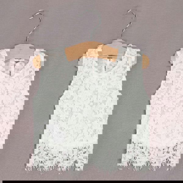 White lace top on a wooden hanger against a gray background