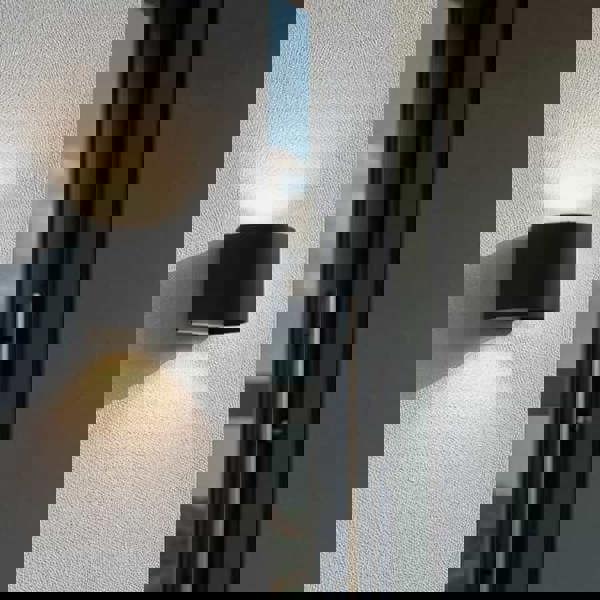 black up down outside light fitted on a white textured wall next to the entrance door of a modern home