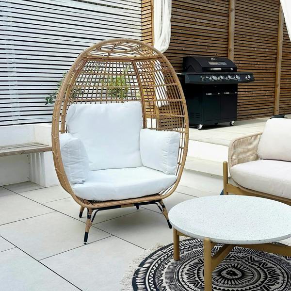 Khaki rattan egg chair with white seat cushion and back cushion in an outdoor setting