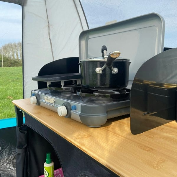 The OLPRO Deluxe Camp Kitchen With Double Cupboard pictured with a stove on top of it with pans on the stove.