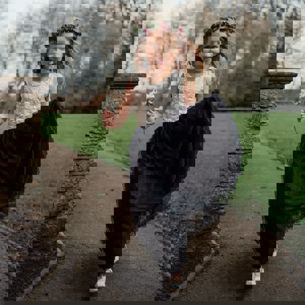 Young girl in a white top and black skirt with a flower crown running outdoors.