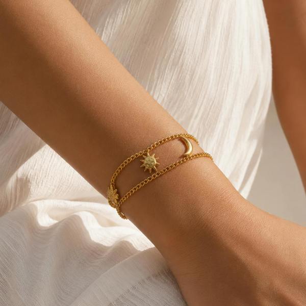 A close-up of a person's wrist wearing a delicate gold double-band bracelet with a star and crescent moon design, styled with a white textured dress.