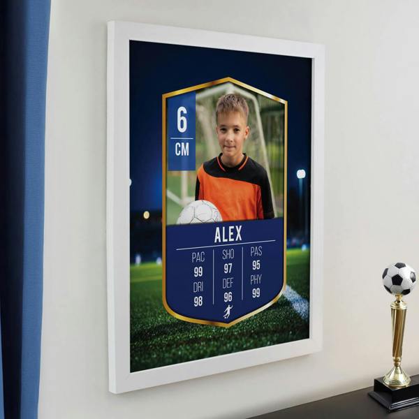 A framed custom ultimate team football card poster hanging on a white wall in a bedroom next to a trophy, featuring a photo of a young boy in an orange jersey and the text ALEX along with player stats.