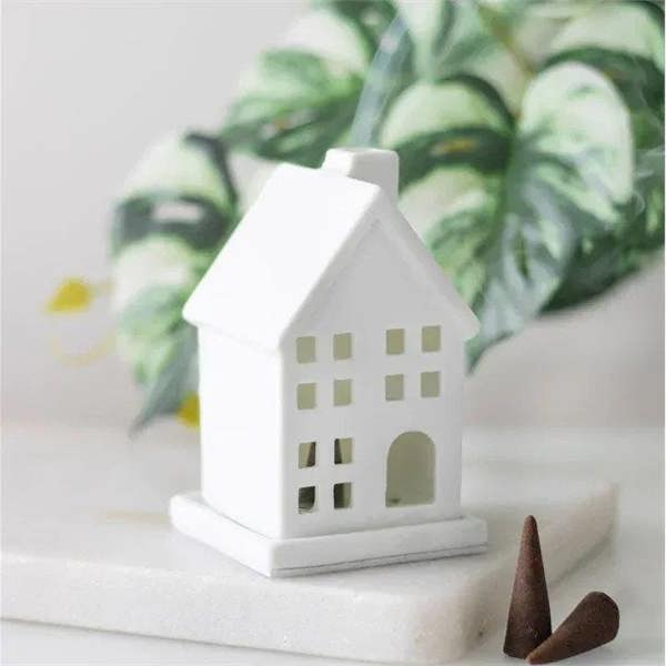 White ceramic house incense cone holder with brown incense cones beside it
